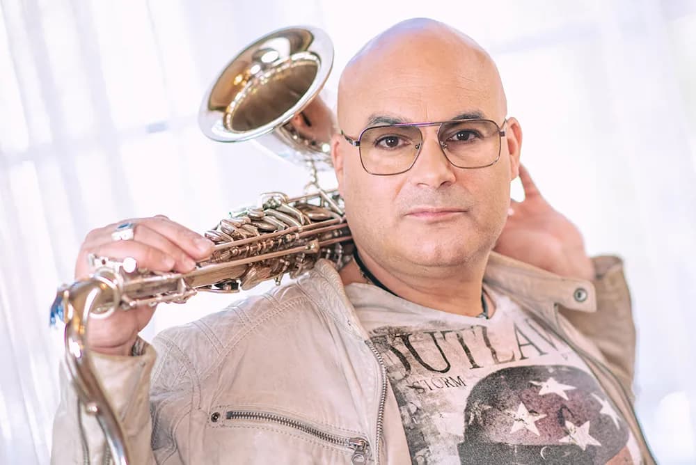 Gianni Bello in heller Lederjacke legt sich ein Saxophon über die Schulter.