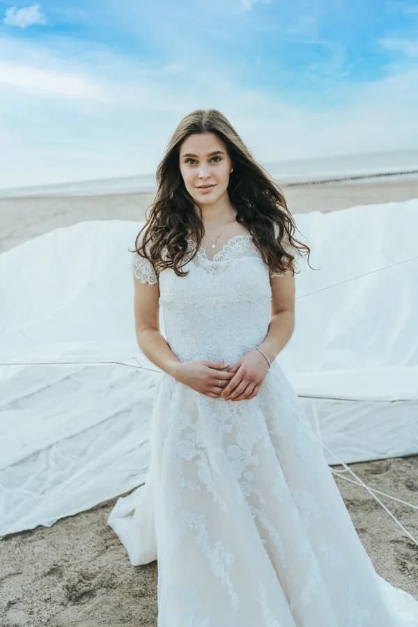 Braut im weißen Spitzenkleid am Strand, dahinter ein aufgespanntes weißes Segeltuch.