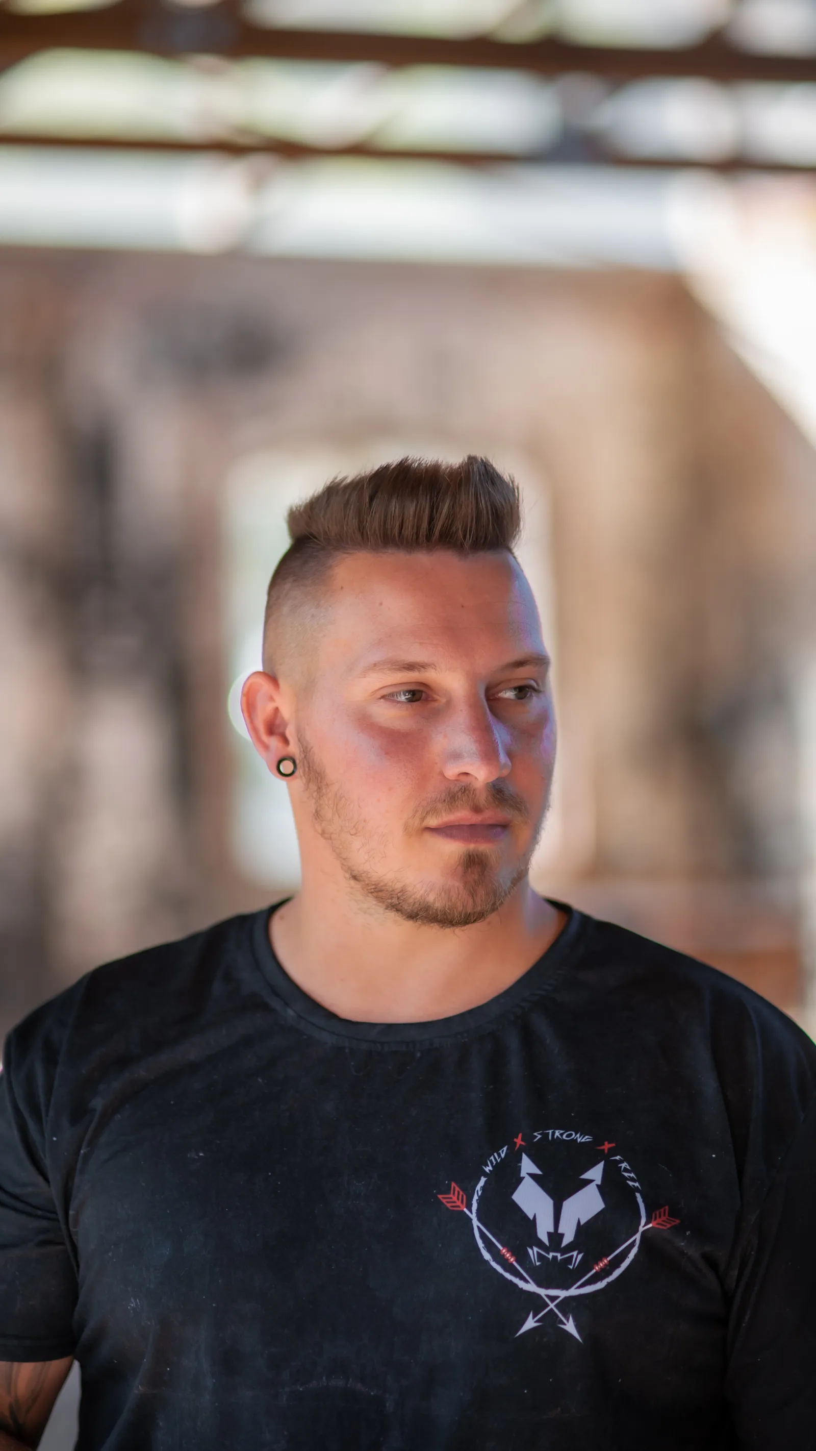 Junger Mann mit Undercut im schwarzen Shirt, Blick zur Seite, Hintergrund unscharf.