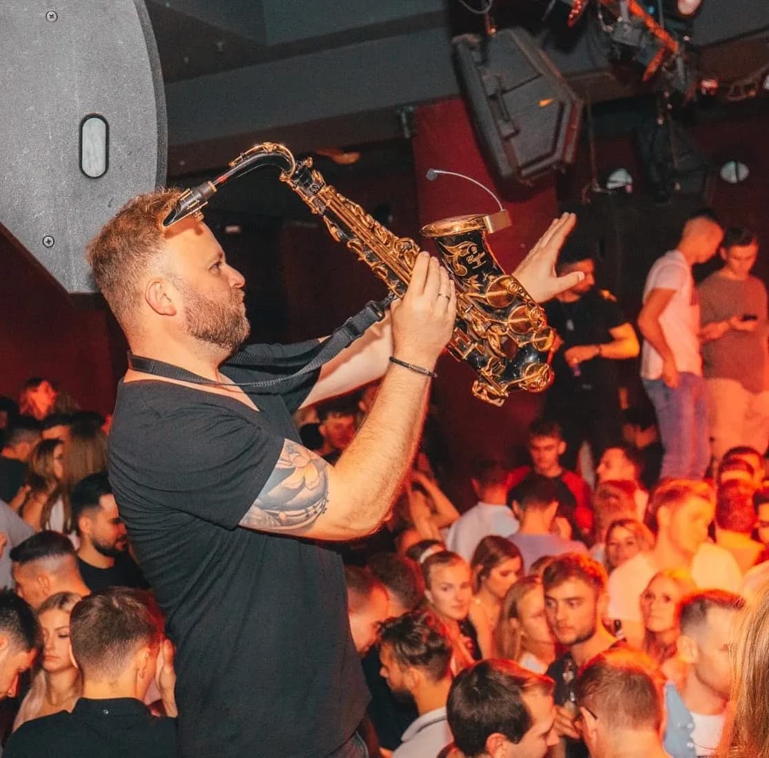DimiSaxx spielt Saxophon im Club, umgeben von Publikum im roten Licht.
