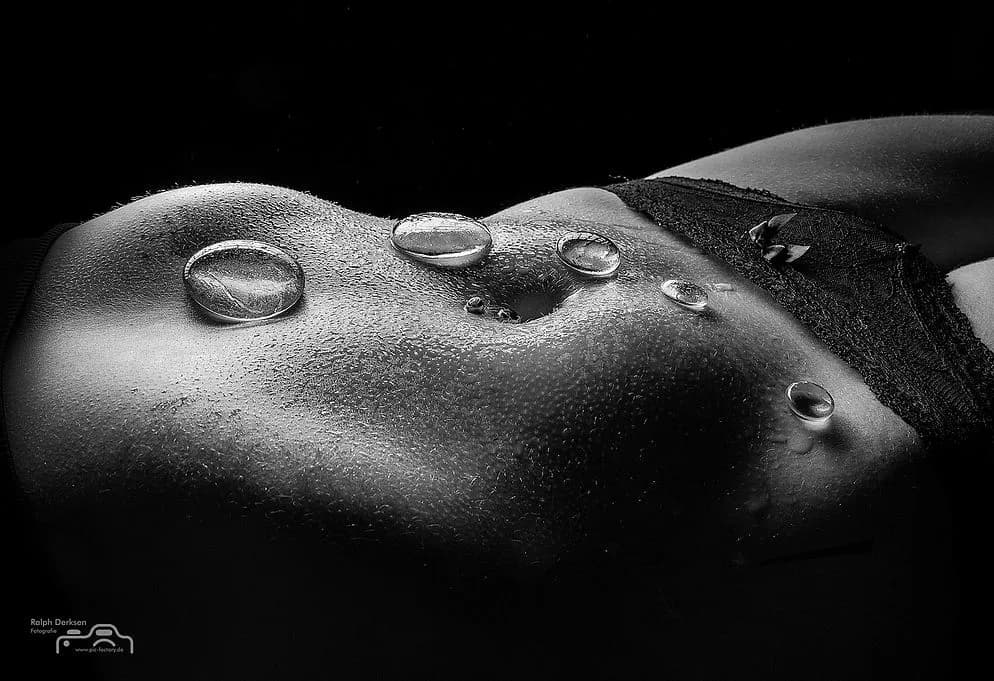 Schwarz-Weiß-Detailaufnahme: Wassertropfen auf Haut, am rechten Rand schwarze Spitze.
