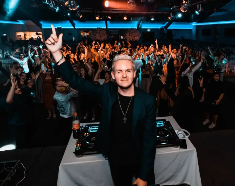 Tim Twice hinter dem DJ-Pult mit erhobenem Arm, dahinter Publikum mit erhobenen Händen.
