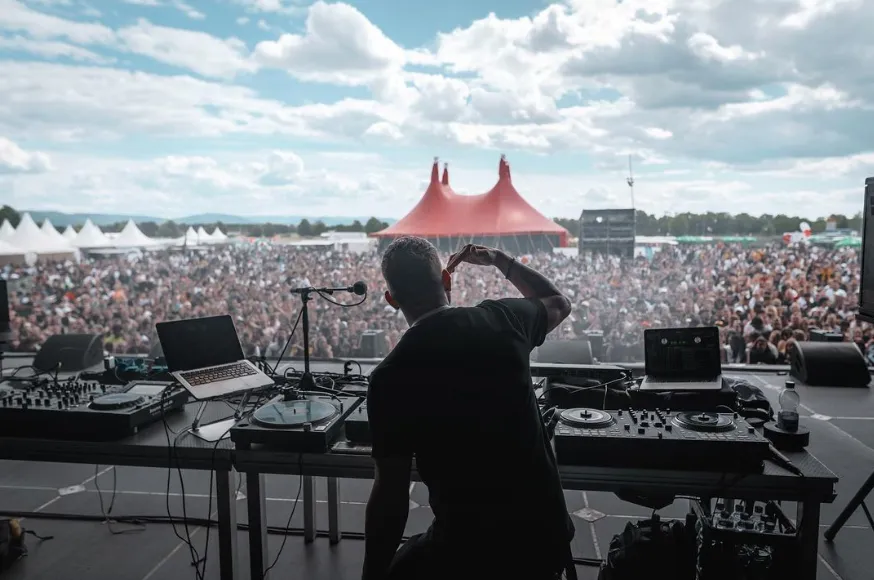 DJ von hinten am Pult einer Open-Air-Bühne, davor große Menschenmenge und rotes Zelt.