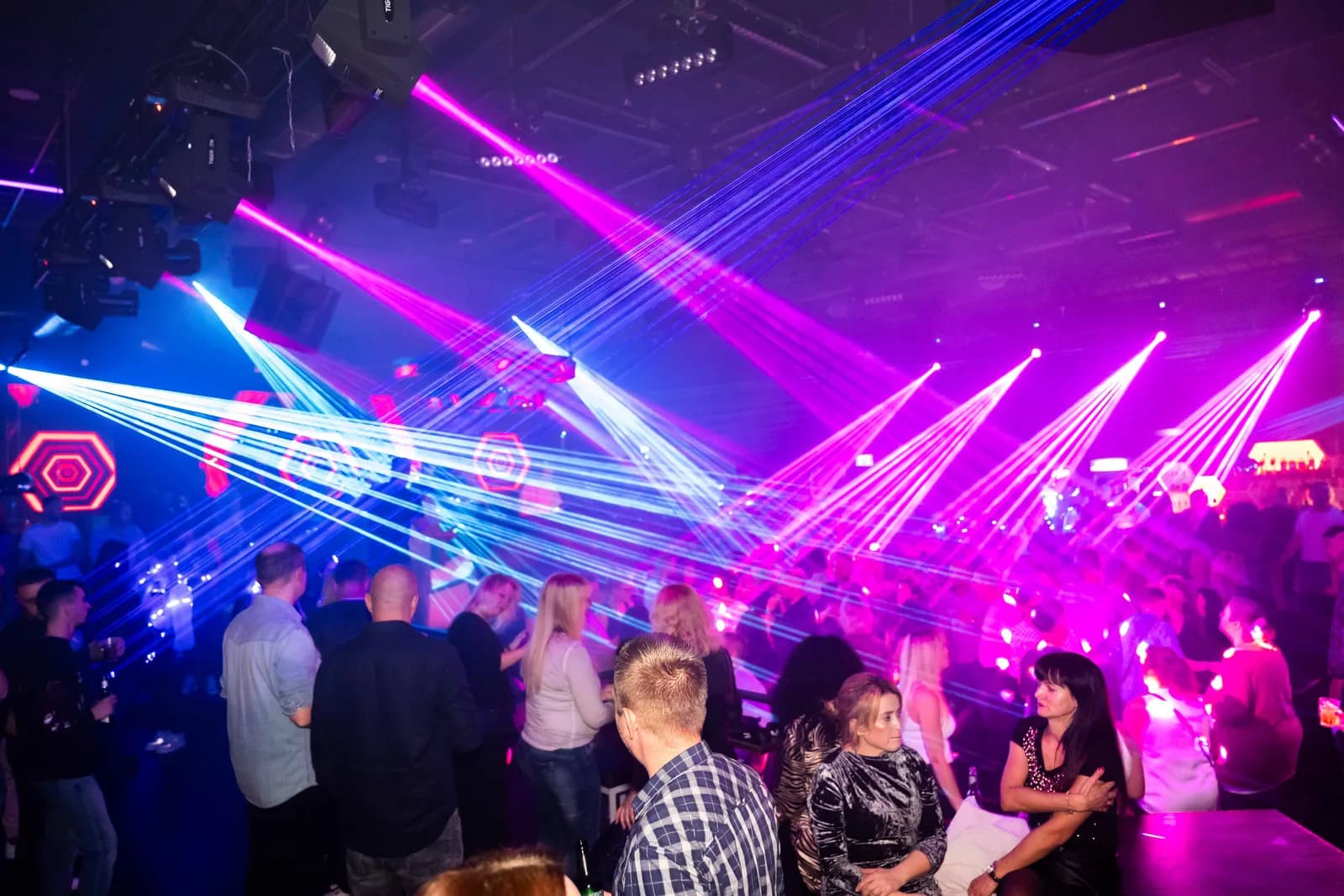 Clubnacht mit blauen und pinken Laserfächern über der Tanzfläche voller Gäste.