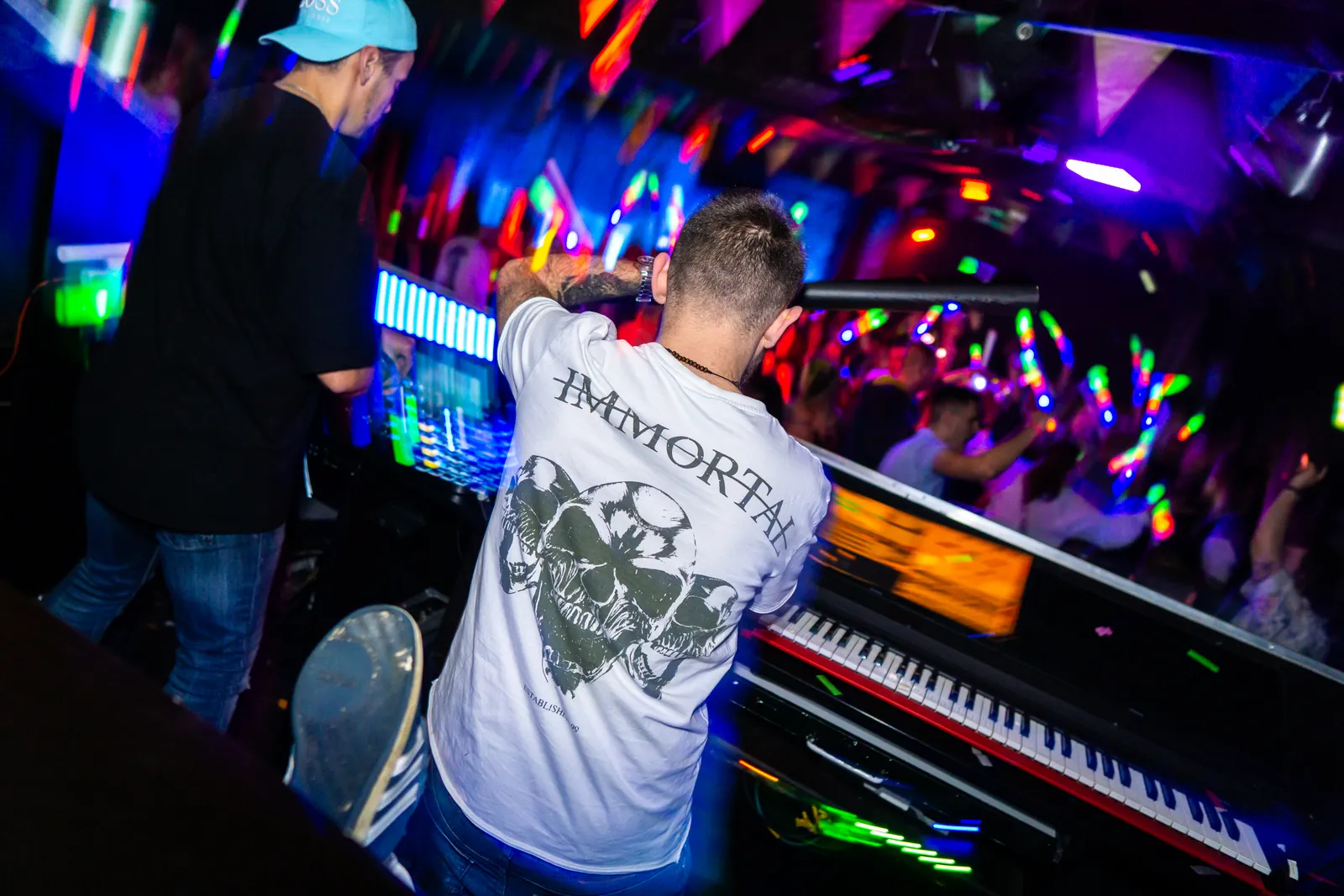 Blick von hinten auf das DJ-Pult, ein Musiker am Keyboard, unten Publikum mit Leuchtstäben.