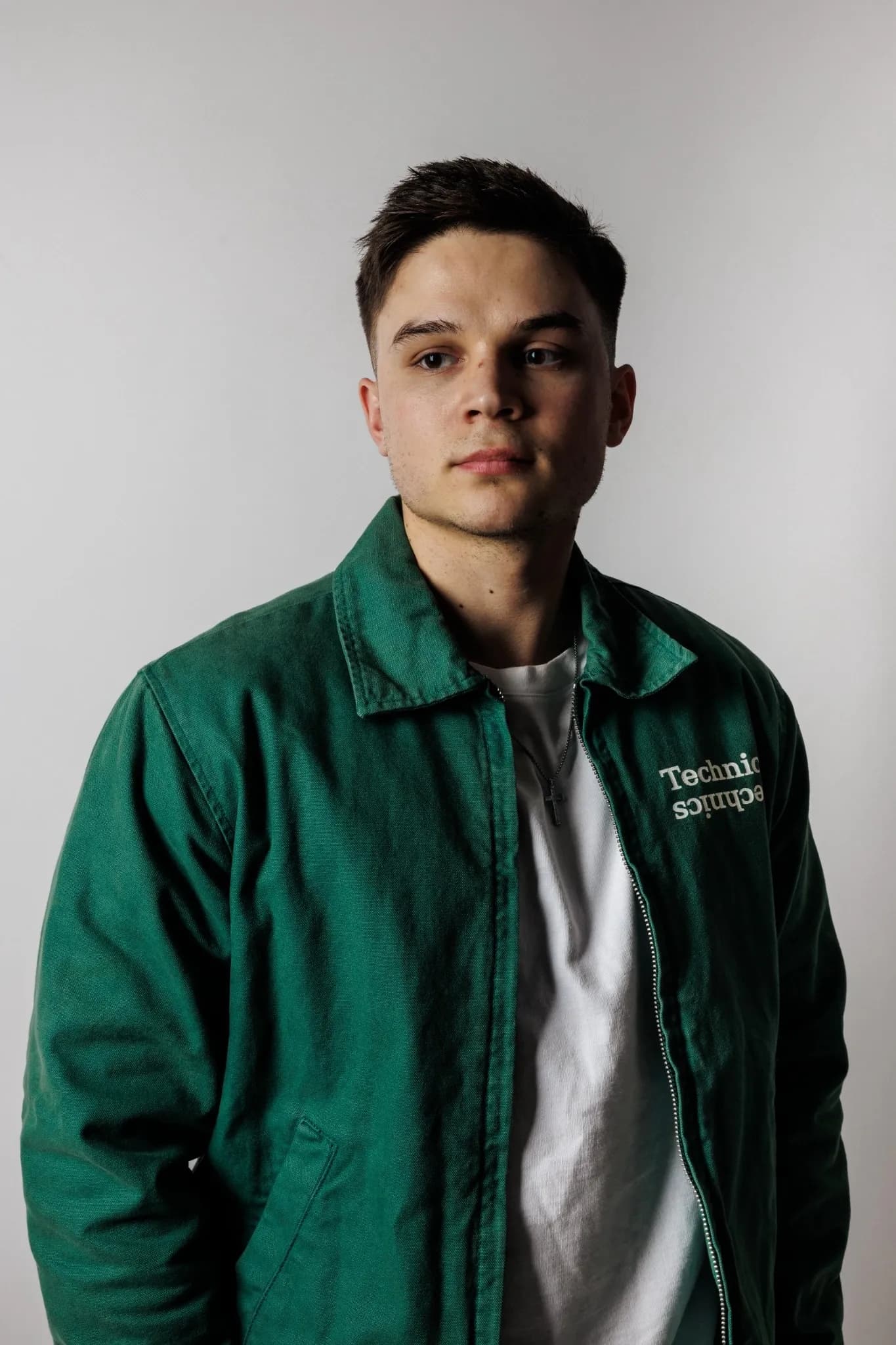 Junger Mann in grüner Jacke mit Technics-Schriftzug vor hellgrauem Studiohintergrund.
