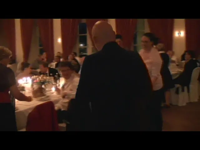 Dunkler Saal mit gedeckten Tischen und Gästen, ein Mann im Anzug geht zwischen den Tischen hindurch.