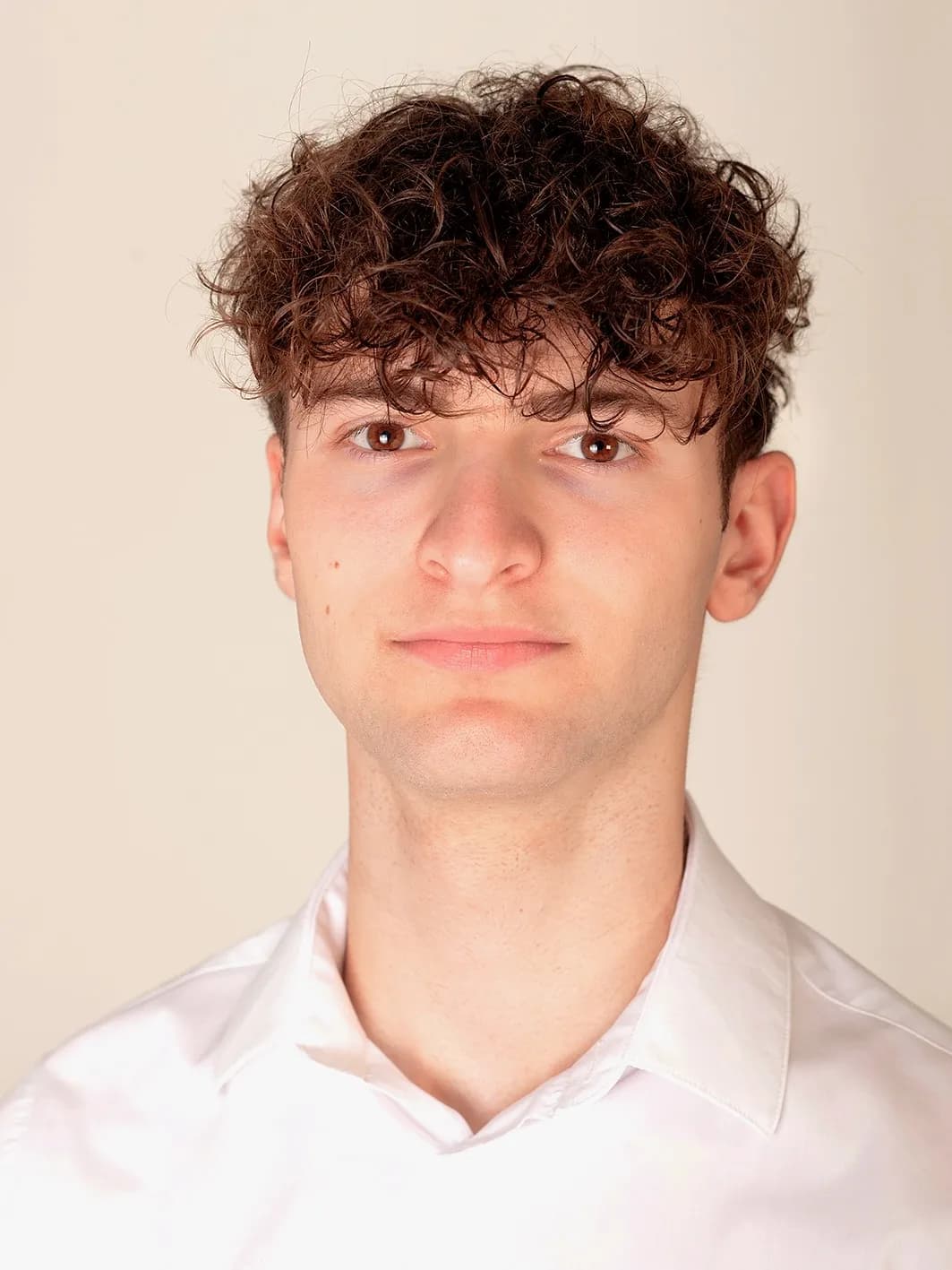 Justus von Justus Films mit dunklen Locken im weißen Hemd vor beigem Hintergrund.