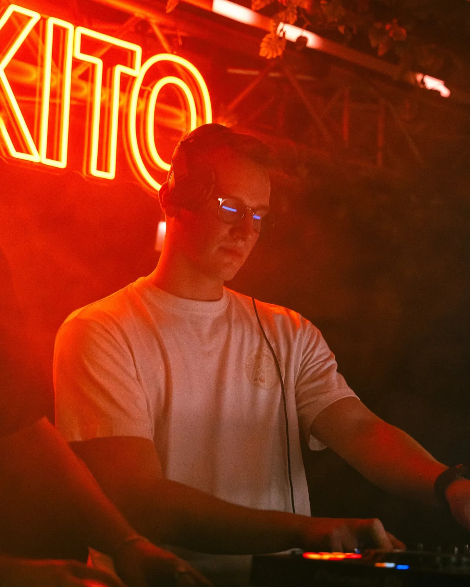 DJ Urmel mit Kopfhörern am Pult, dahinter rote Leuchtschrift mit den Buchstaben KITO.