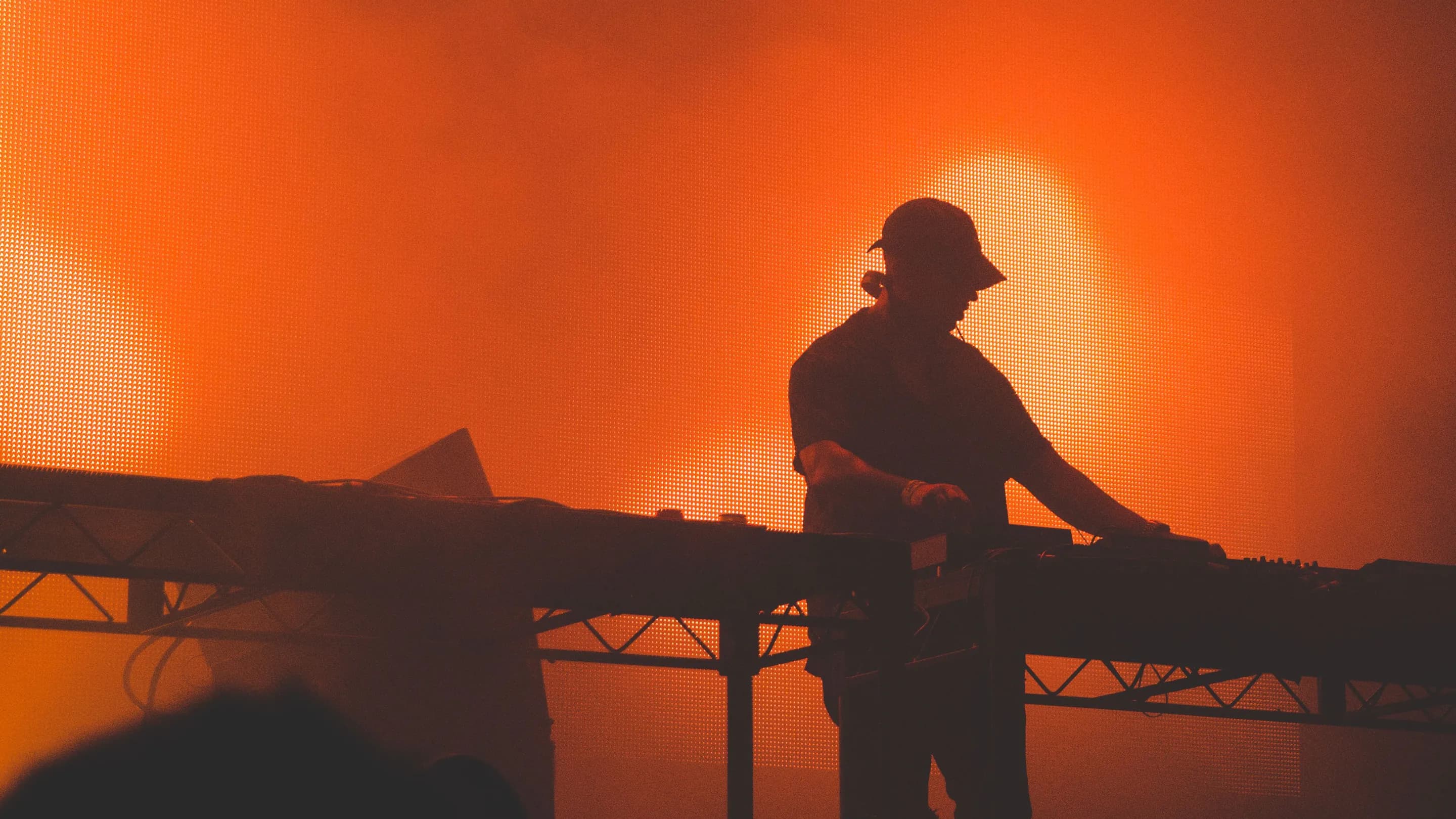 Ein DJ als Silhouette am Pult vor einer orange leuchtenden LED-Wand im Bühnennebel.